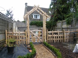 Pitched roof chestnut rose arch with leaf gate and paling fence