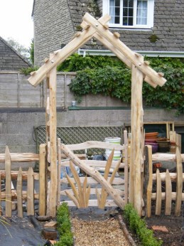 Pitched roof chestnut rose arch with leaf gate and paling fence